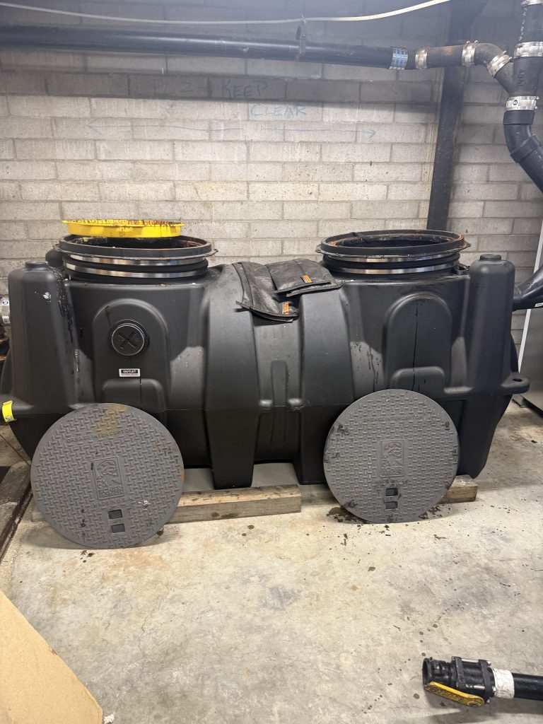 Commercial grease interceptor installed outdoors in a parking lot near restaurant